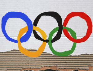 Ein Pappschild mit den fünf Olympischen Ringen, die in den Farben blau, schwarz, rot, gelb und grün etwas unregelmäßig ausgemalt sind.