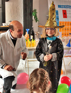 Ein Junge im Magier-Kostüm führt ein Experiment vor, assistiert von Robert Mingau in seiner Rolle als Chemie-Professor