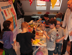 Kinder stehen um einen Labortisch in einer Wohnung und experimentieren