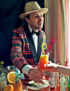 Spielleiter Robert Mingau als Barkeeper überreicht einen Cocktail an eine Kinderhand