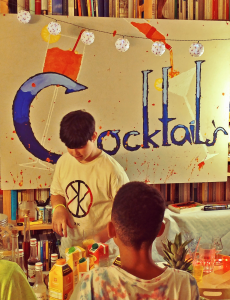 Cocktailbar-Dekoration mit großem Schild und Lampionkette, einige Kinder mixen sich Drinks