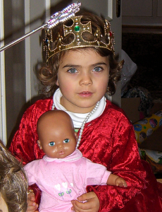 ein etwa vierjähriges Mädchen im samtroten Prinzessinnen-Kleid mit einer Puppe im Arm