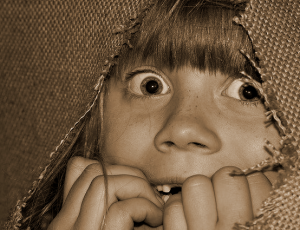ein Kind schaut mit weit aufgerissenen Augen aus einem zerrissenen Jutesack heraus