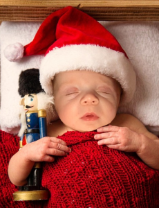 ein Baby mit Weihnachtsmannmütze schläft und hält dabei einen Nussknacker im Arm