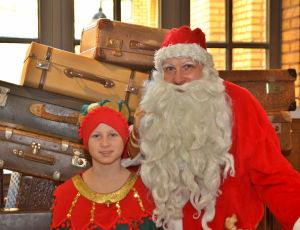 Weihnachtsmann Robert Mingau und Weihnachtself Zimtstern vor einem Stapel alter Reisekoffer